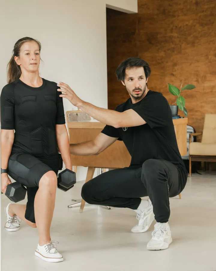 Trener koryguje pozycję klientki w kombinezonie EMS podczas treningu w studiu