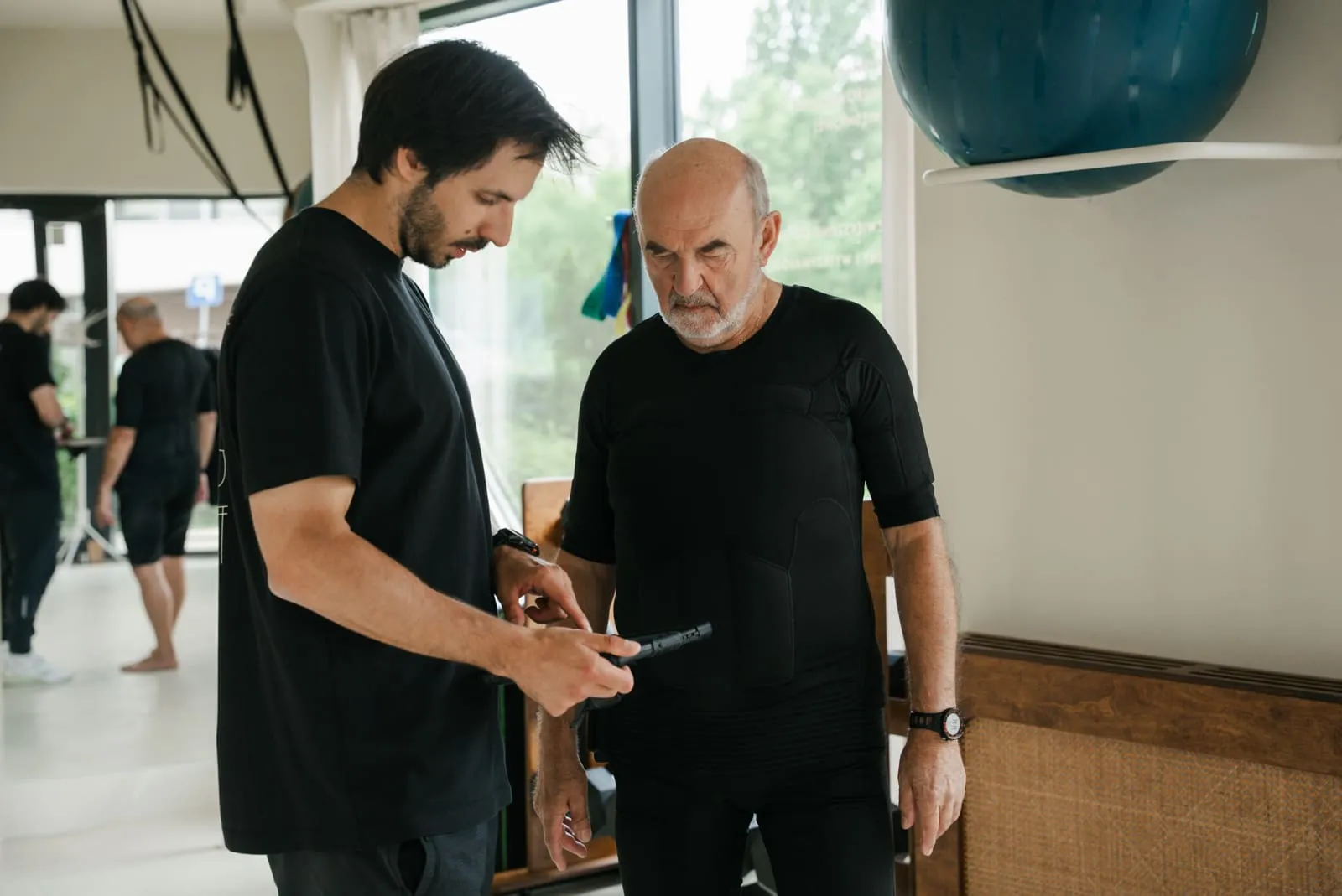 Trener ustawia parametry urządzenia EMS przed treningiem starszego klienta