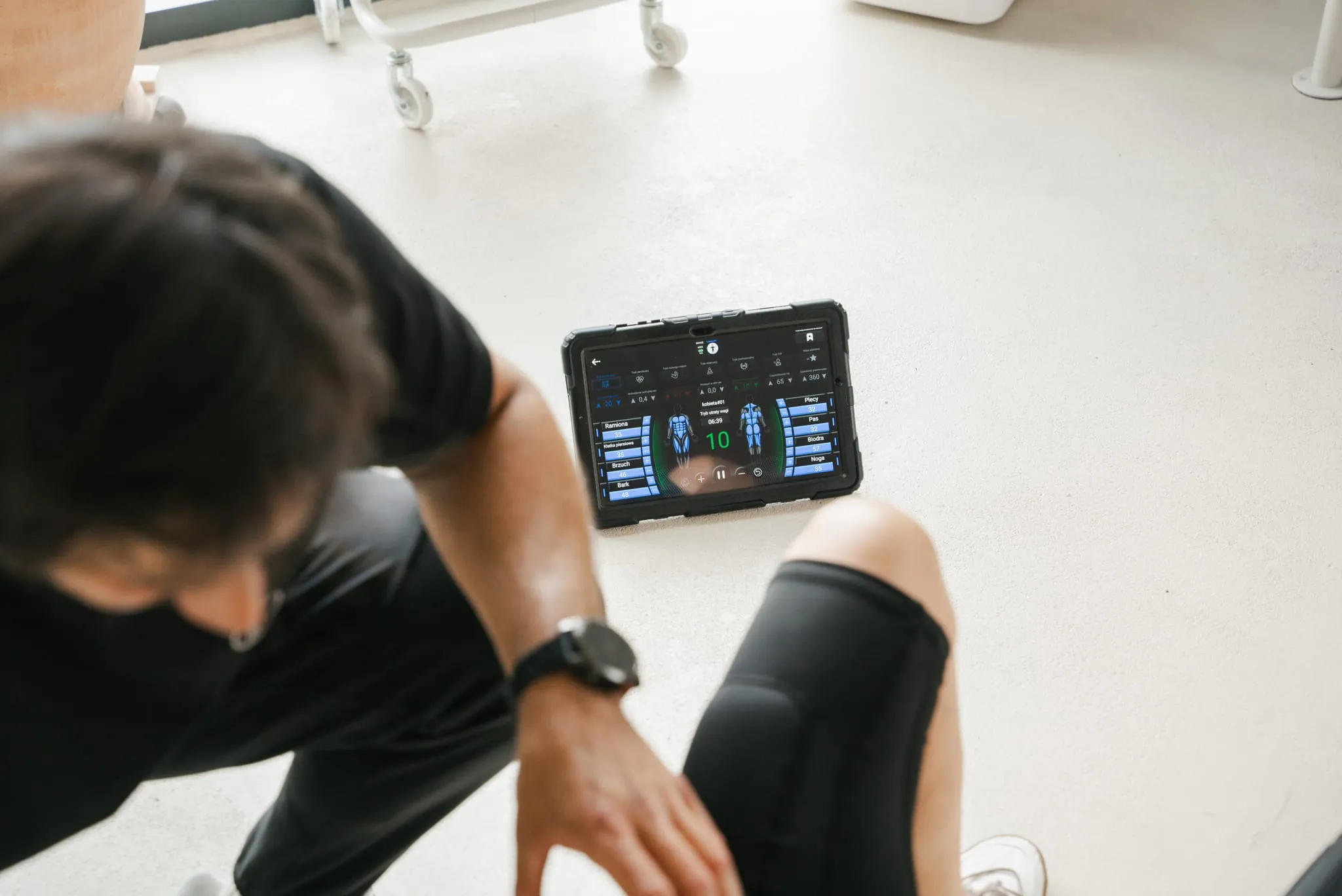 Tablet ze sterowaniem urządzenia EMS na podłodze studia, trener ustawia parametry