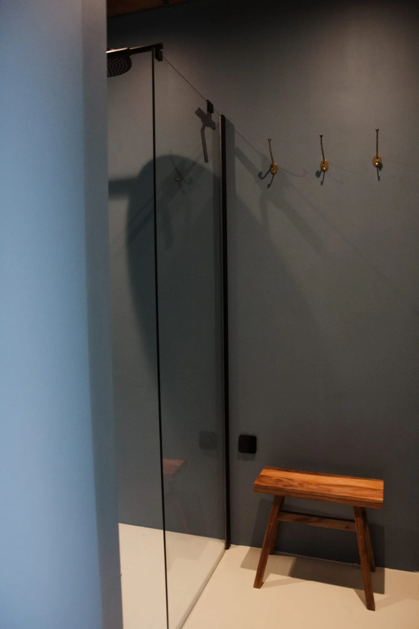 Prysznic za szklaną ścianką, mosiężne wieszaki i drewniany taboret w łazience studia