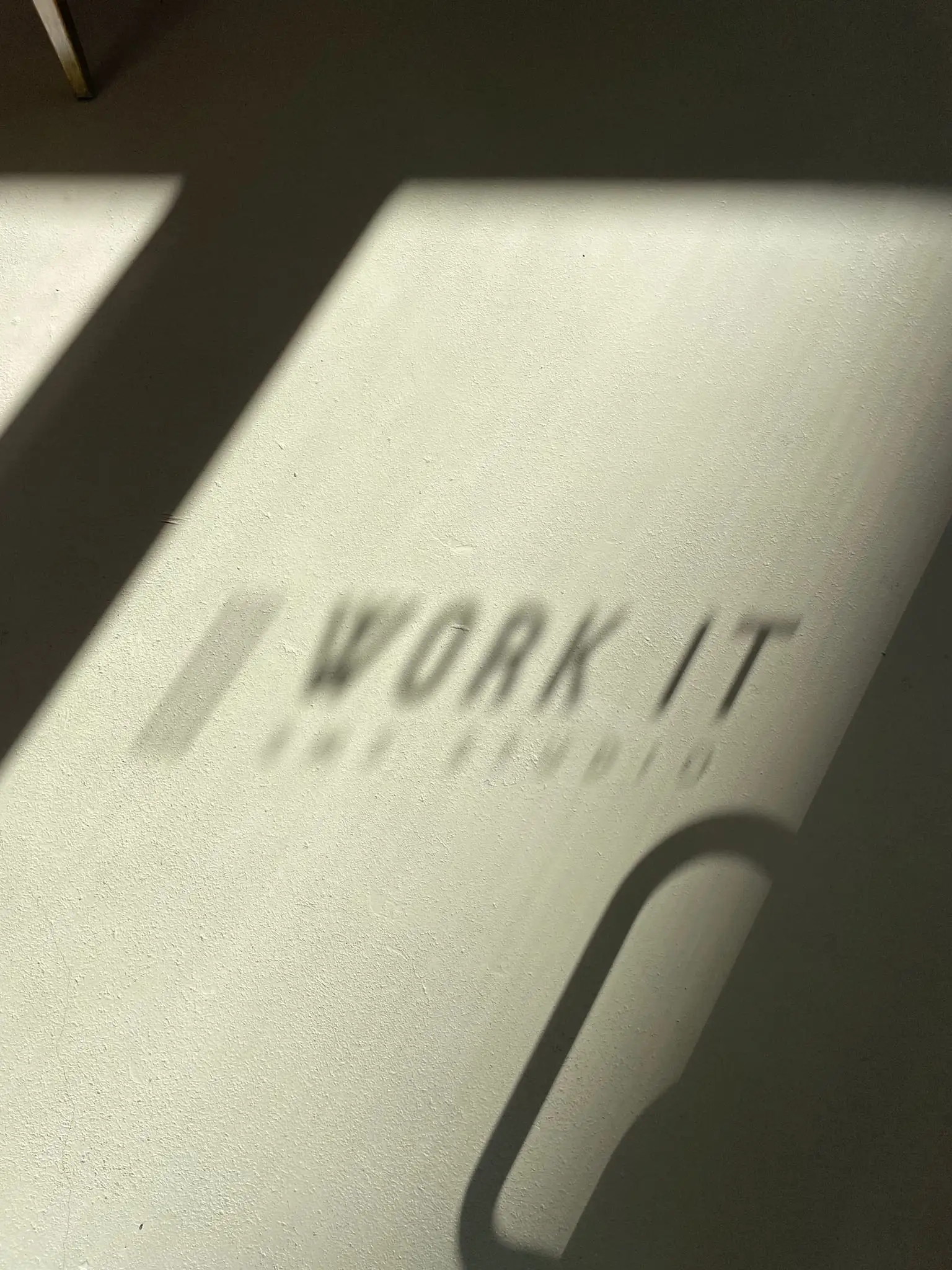 Cień logo WORK IT EMS rzucony przez światło na ścianę studia